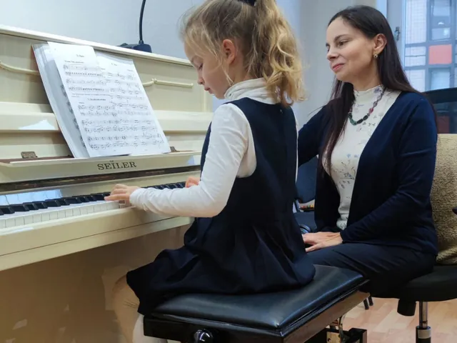 Ein Mädchen spielt Klavier, die Lehrkraft sitzt daneben und hört zu